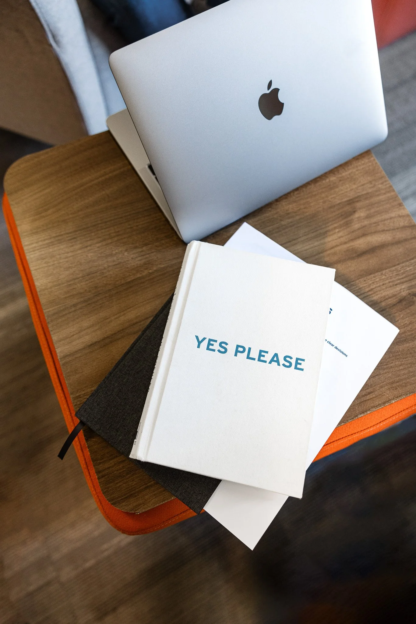 A small table with a silver laptop and the book "Yes Please".