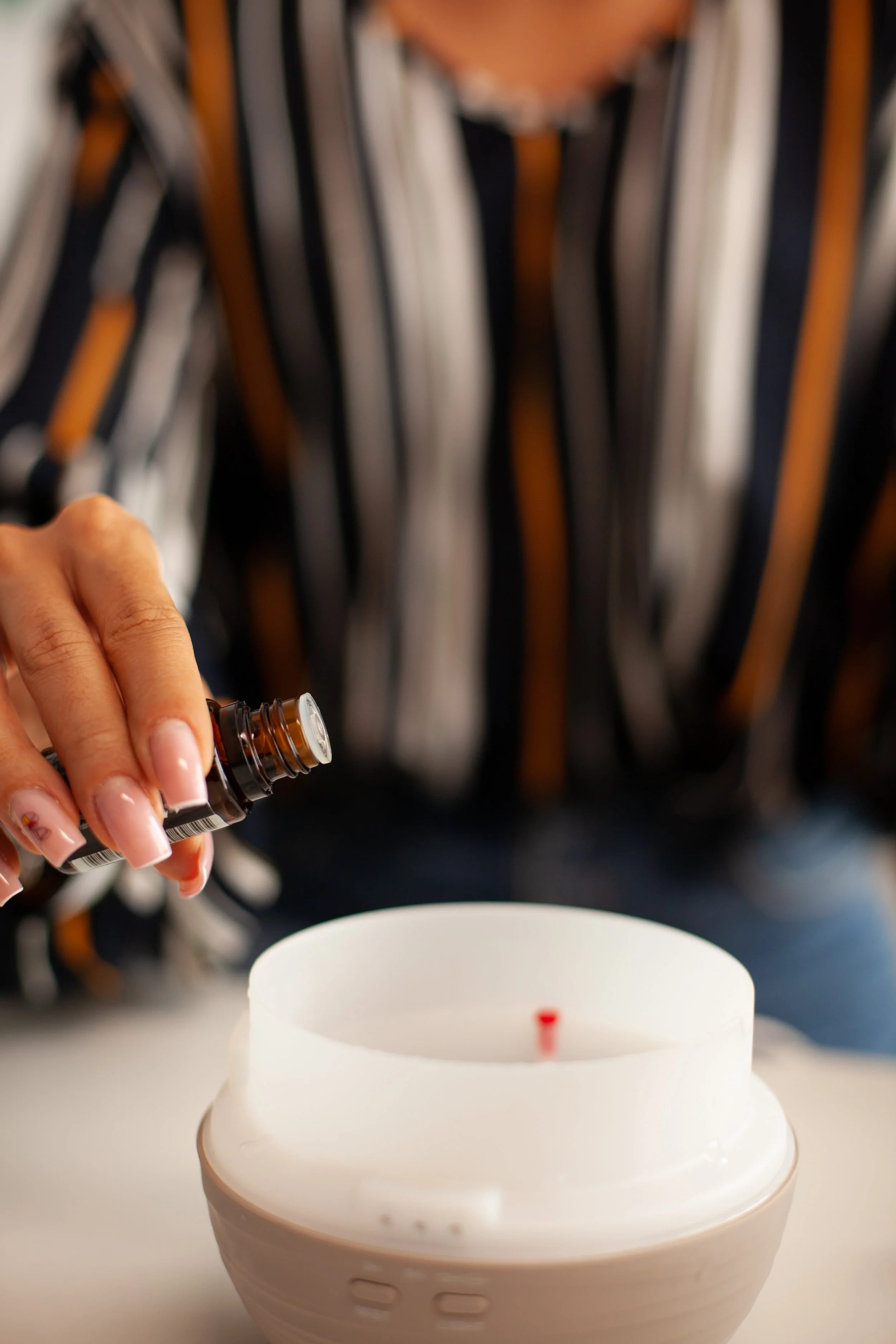 A person holding a small amber bottle above a white birthday cake with a single red candle on top.