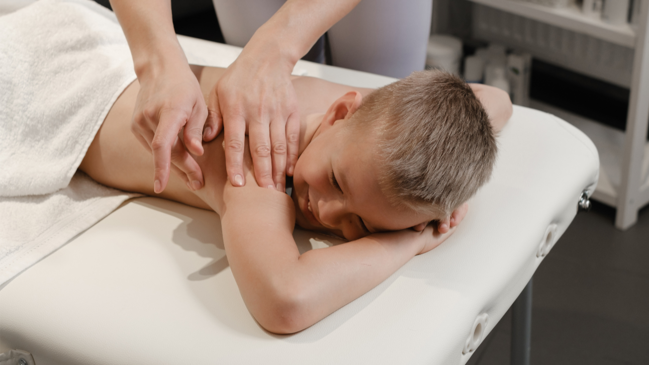 Child receiving a back massage from a massage therapist in a wellness center.