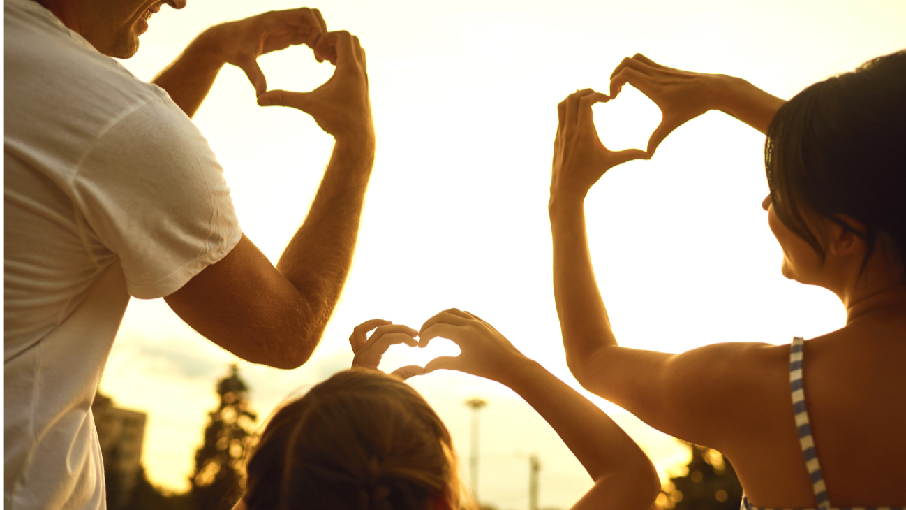 Family Time! making heart shapes with their hands against a sunset background.