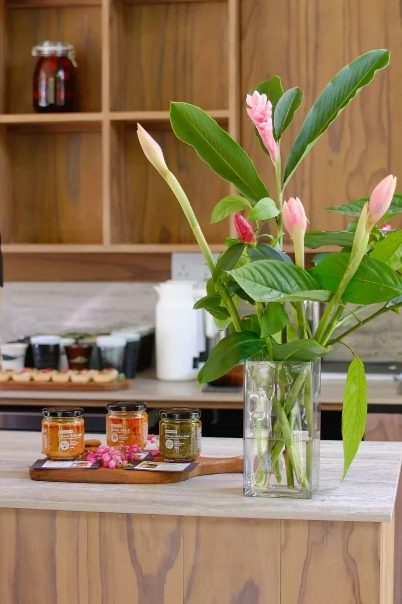 A glass vase containing a pink flowering plant on a wooden counter in a kitchen.