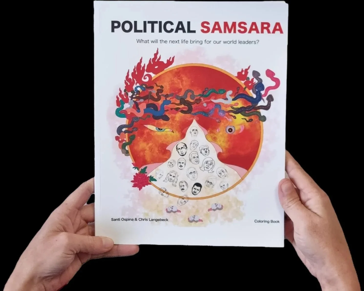 A person holding a coloring book titled "POLITICAL SAMSARA" with a subtitle "What will the next life bring for our world leaders?" The cover features an illustration of a fiery sun with swirling multicolored snakes, a small eye, and a flame, with a pyramid of faces at the bottom. The authors are Santi Ospina and Chris Langebeck.