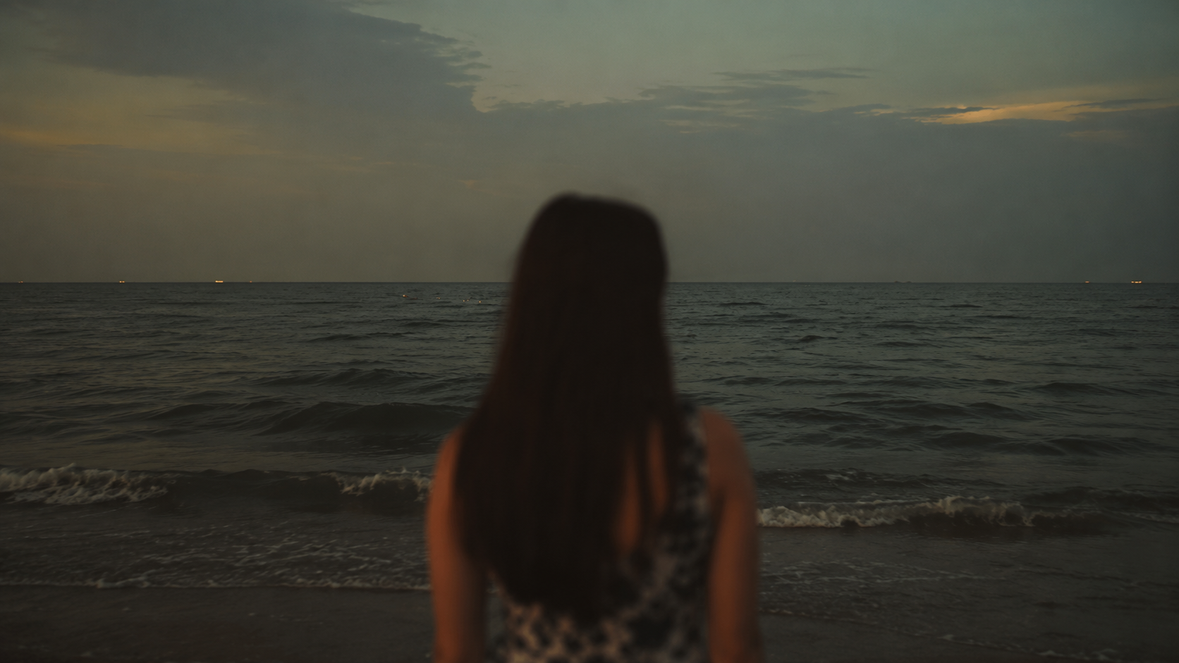 A solitary figure stands before the dark sea at dusk, evoking the longing, memory, and impossibility of returning in Un retorno.