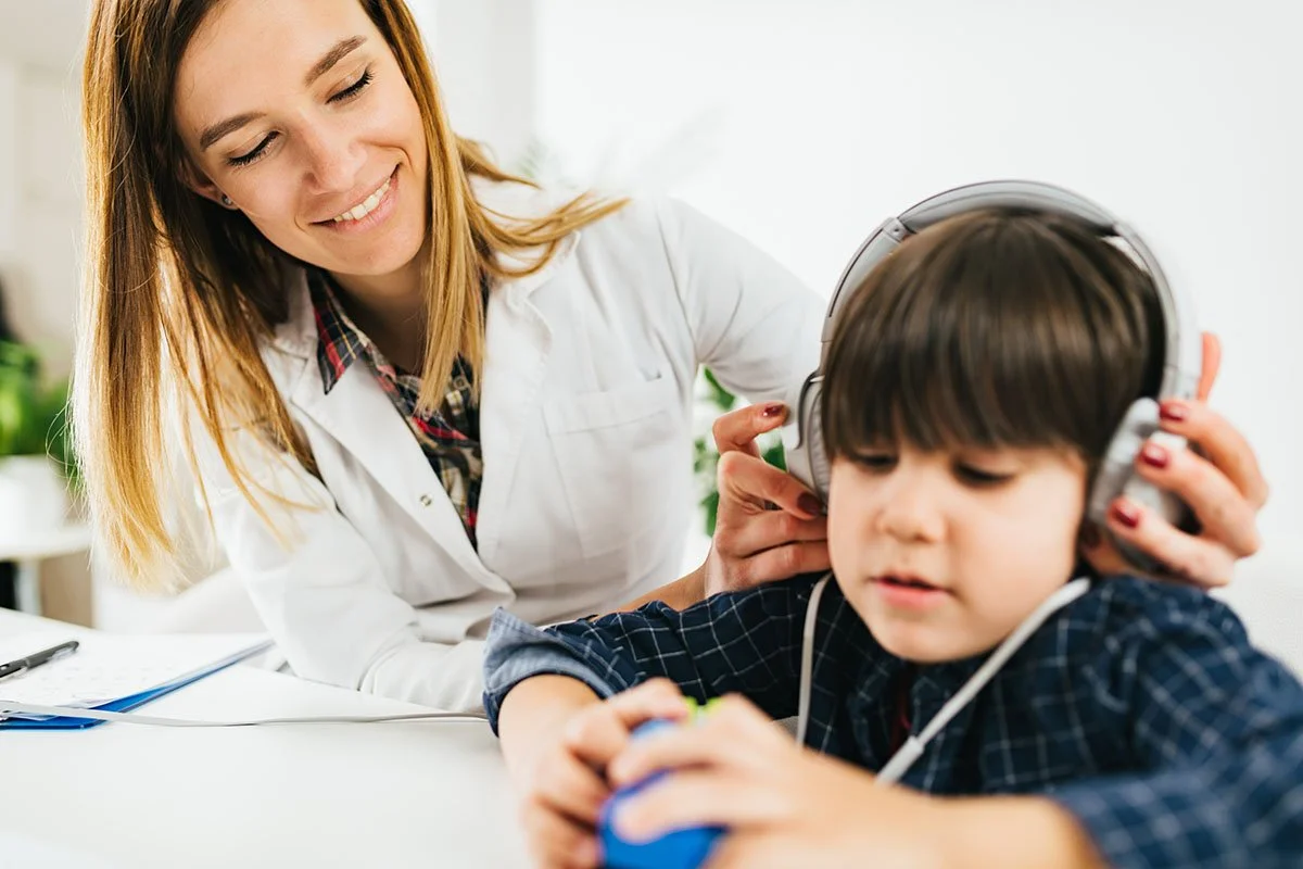 Young woman assisting child with headphones, indoor setting