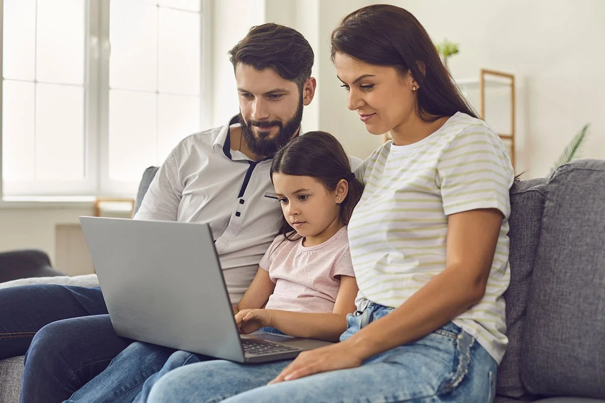 Family of three using a laptop on a couch, smiling and engaged.
