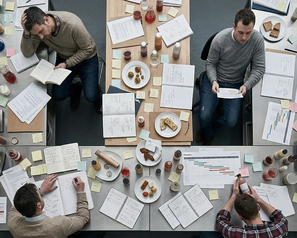 Overhead view of product development team working with notes, samples, and reports during a strategy session.
