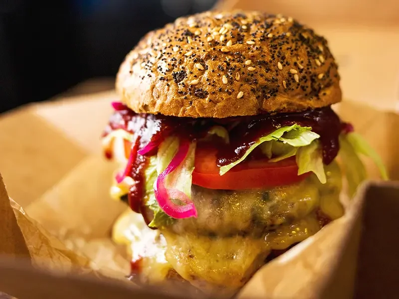 Close-up of a gourmet cheeseburger with fresh toppings and seeded bun, highlighting how menu development services create innovative, sustainable, and commercially successful menu items for modern food brands.