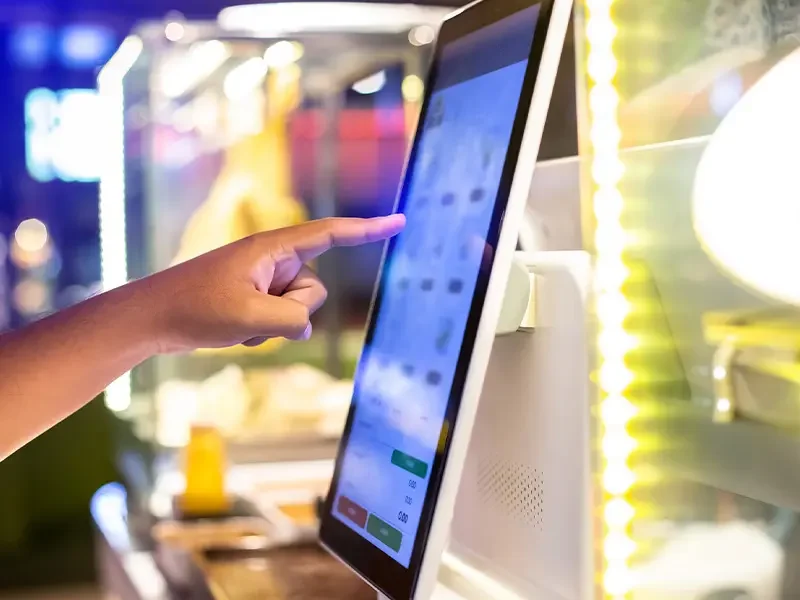 Customer using a digital touchscreen kiosk to place an order, representing how menu development services integrate technology, digital ordering, and pricing strategies to enhance the customer experience.