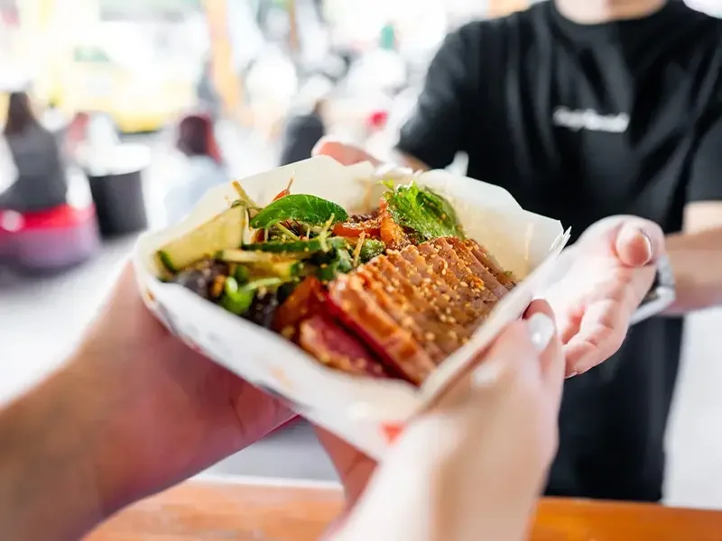 Street food dish being handed to a customer, illustrating how menu development services bring innovative food concepts to market, with menu development services ensuring taste, quality, and consumer appeal.
