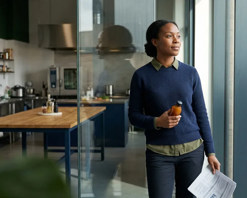 Professional holding a product sample while reviewing a report near a window in a food innovation workspace.