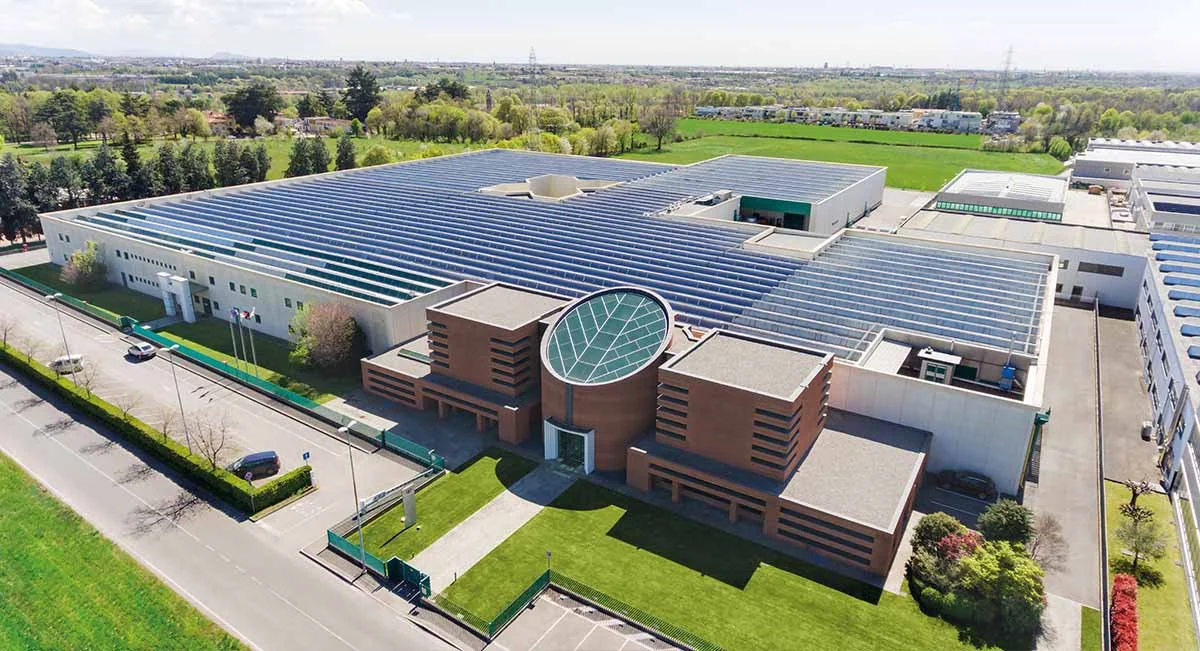 Foto di un grande complesso industriale o aziendale con tetto in vetro e una moderna facciata in mattoni, circondato da zone verdi e strade.