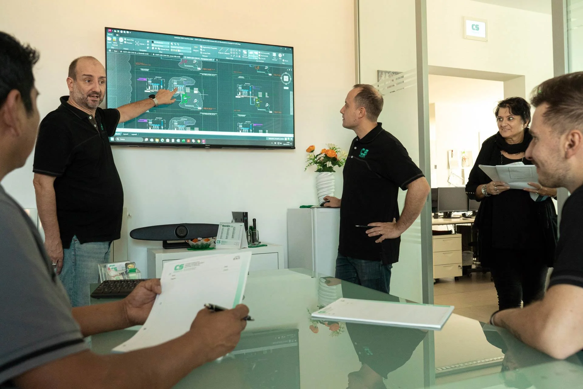 Una riunione aziendale con cinque persone che guardano un diagramma tecnico su uno schermo digitale.