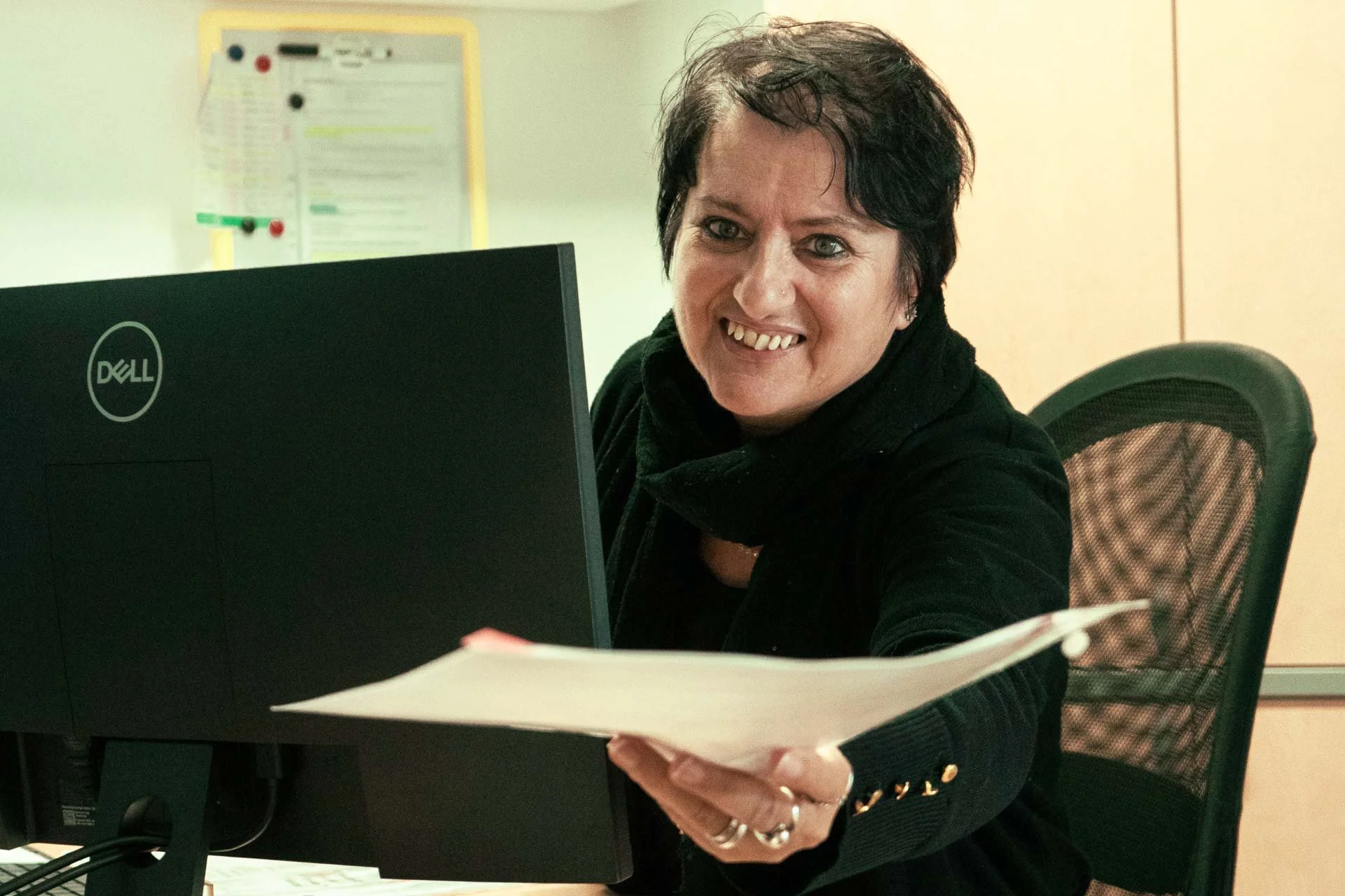 Donna sorridente seduta alla scrivania con un computer Dell e un documento in mano.