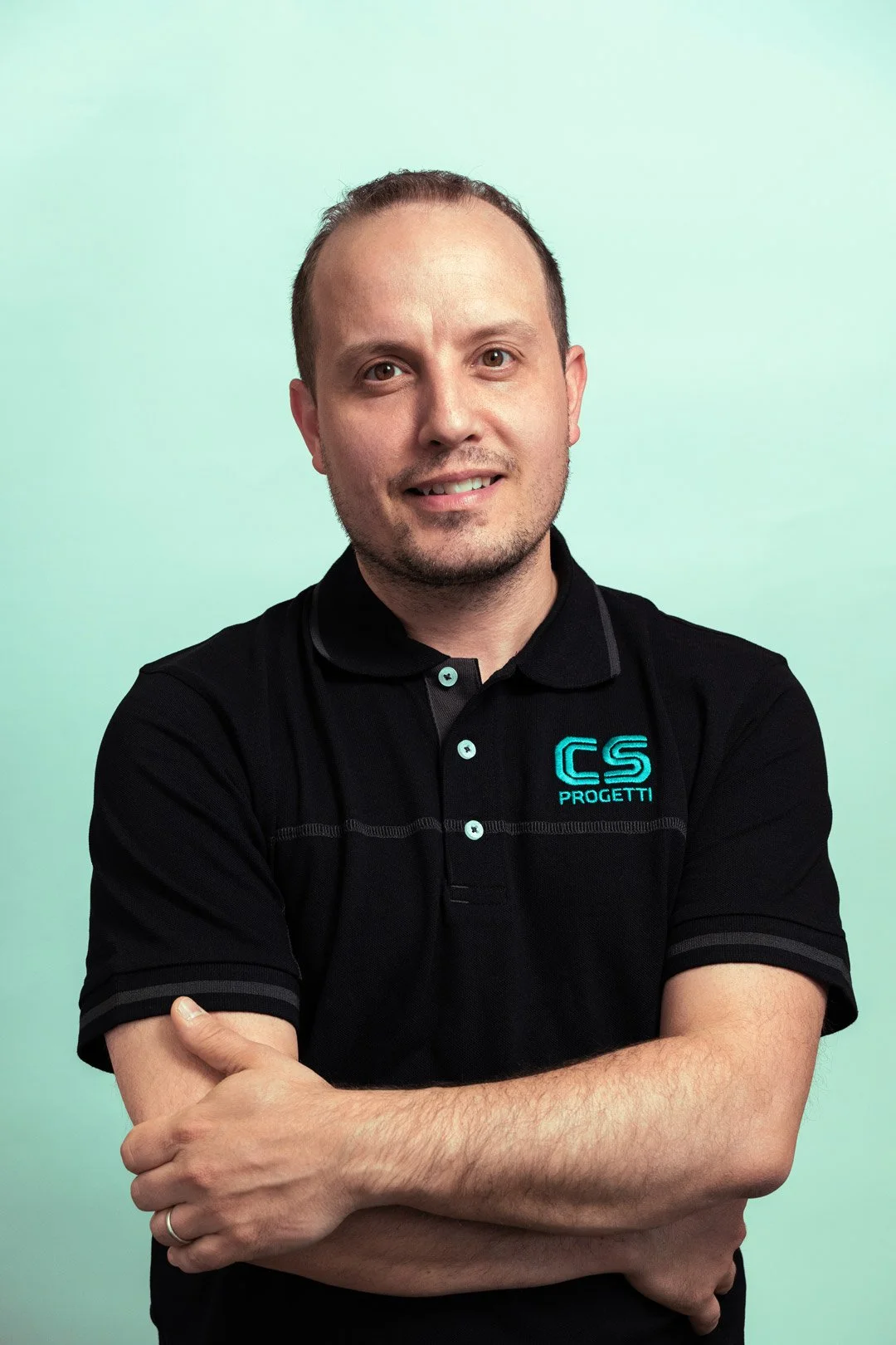 Uomo che indossa una maglietta nera con logo blu 'CS PROGETTI' e sorridente con sfondo verde chiaro.