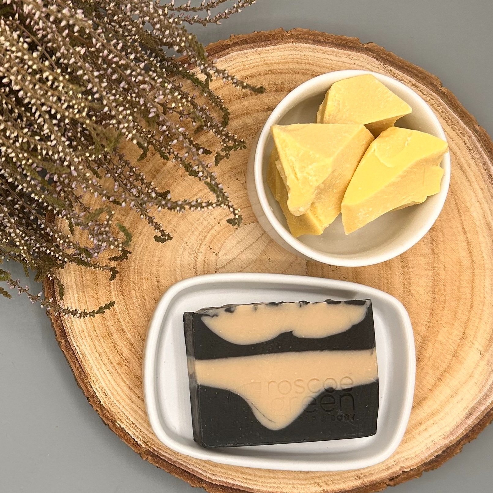 Peppermint, Clove and Activated Charcoal - Cocoa Butter and Clay Natural Soap sat on a wood slice with cocoa butter and heather.