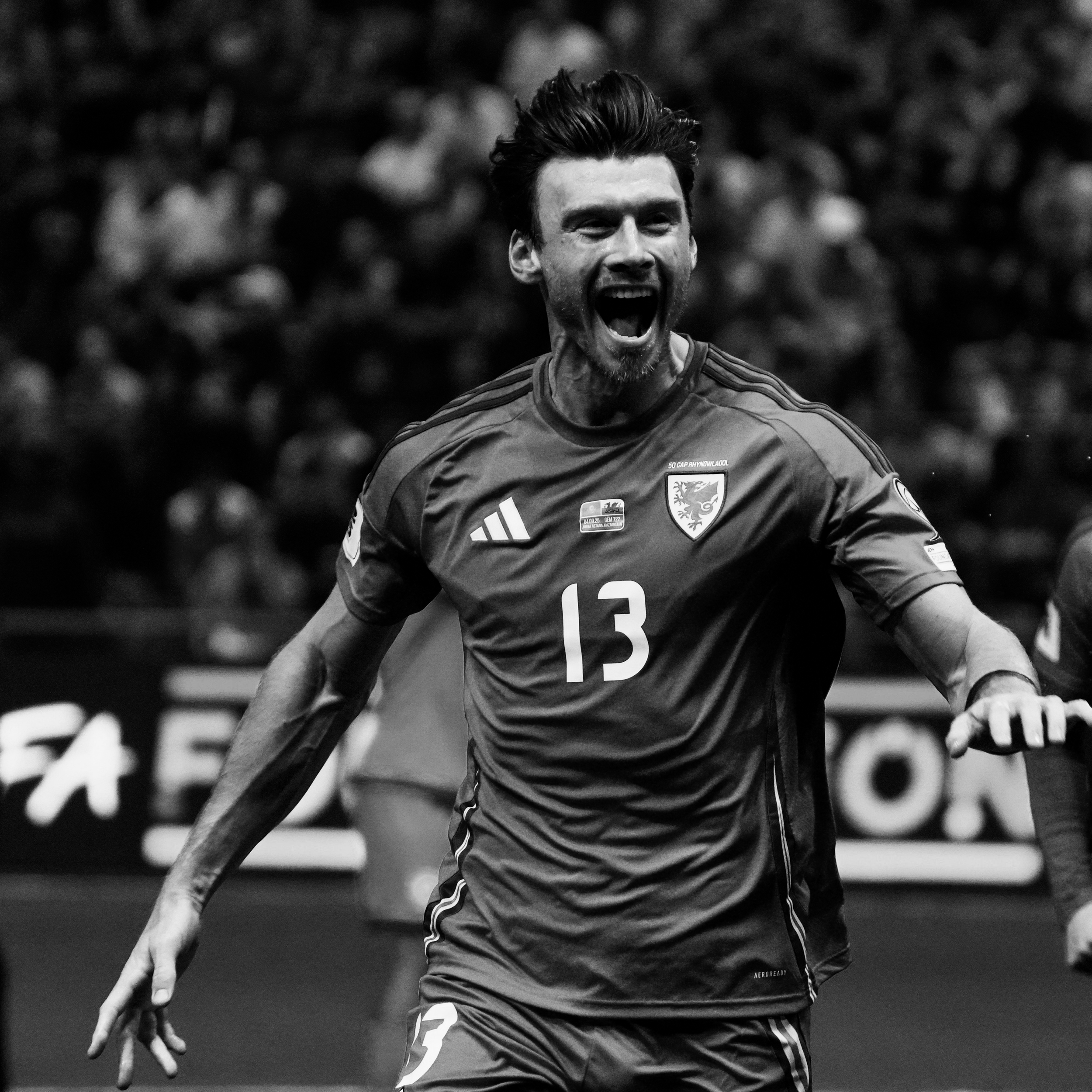 A male soccer player celebrating with his mouth open, wearing a jersey with the number 13 and a crest on the chest, on a soccer field during a match. world cup.