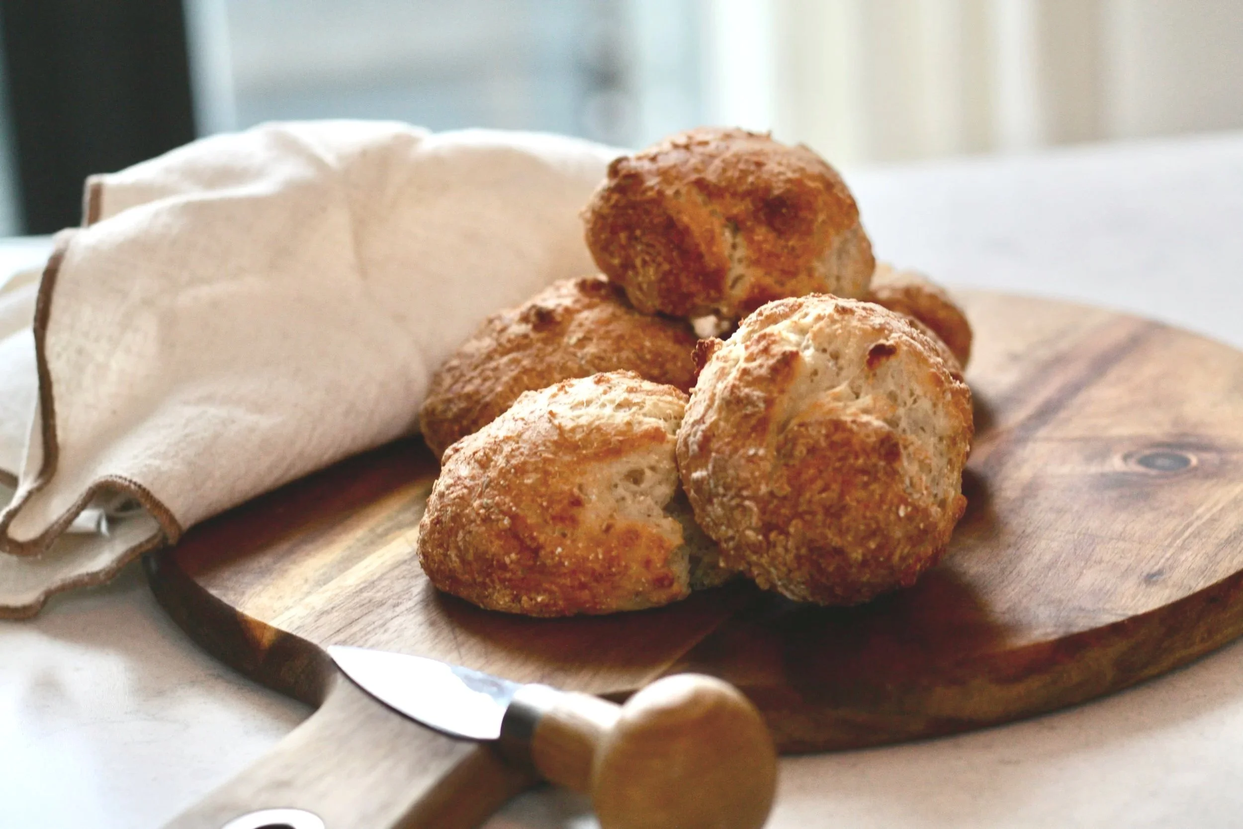 Friterade ostbollar på en träbricka med en kökskniv i förgrunden och en kökshandduk bredvid.