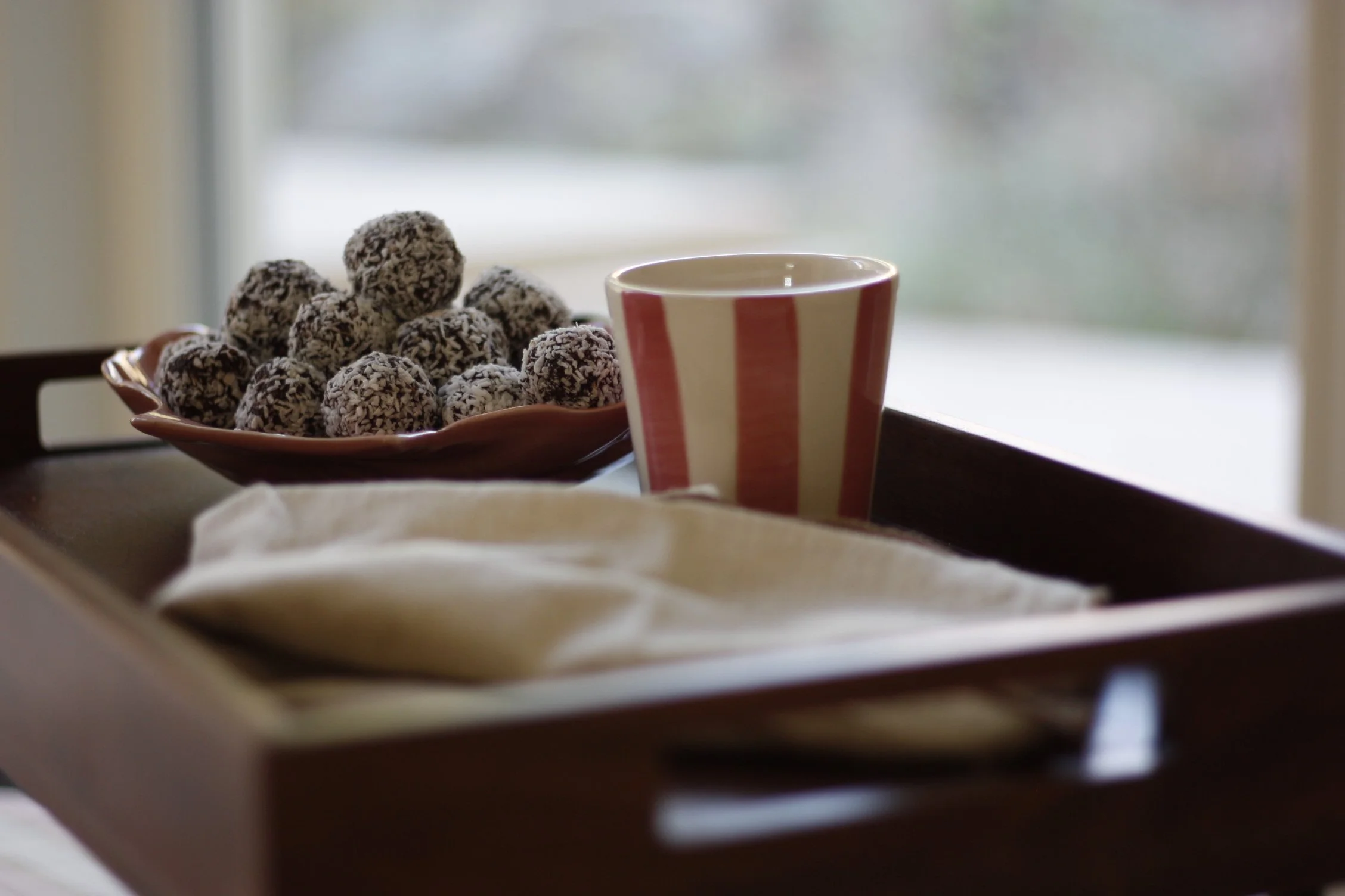 En bricka med chokladkakor täckta av kokosflake, en mugg med röd och vit randig design, och en vit servett.