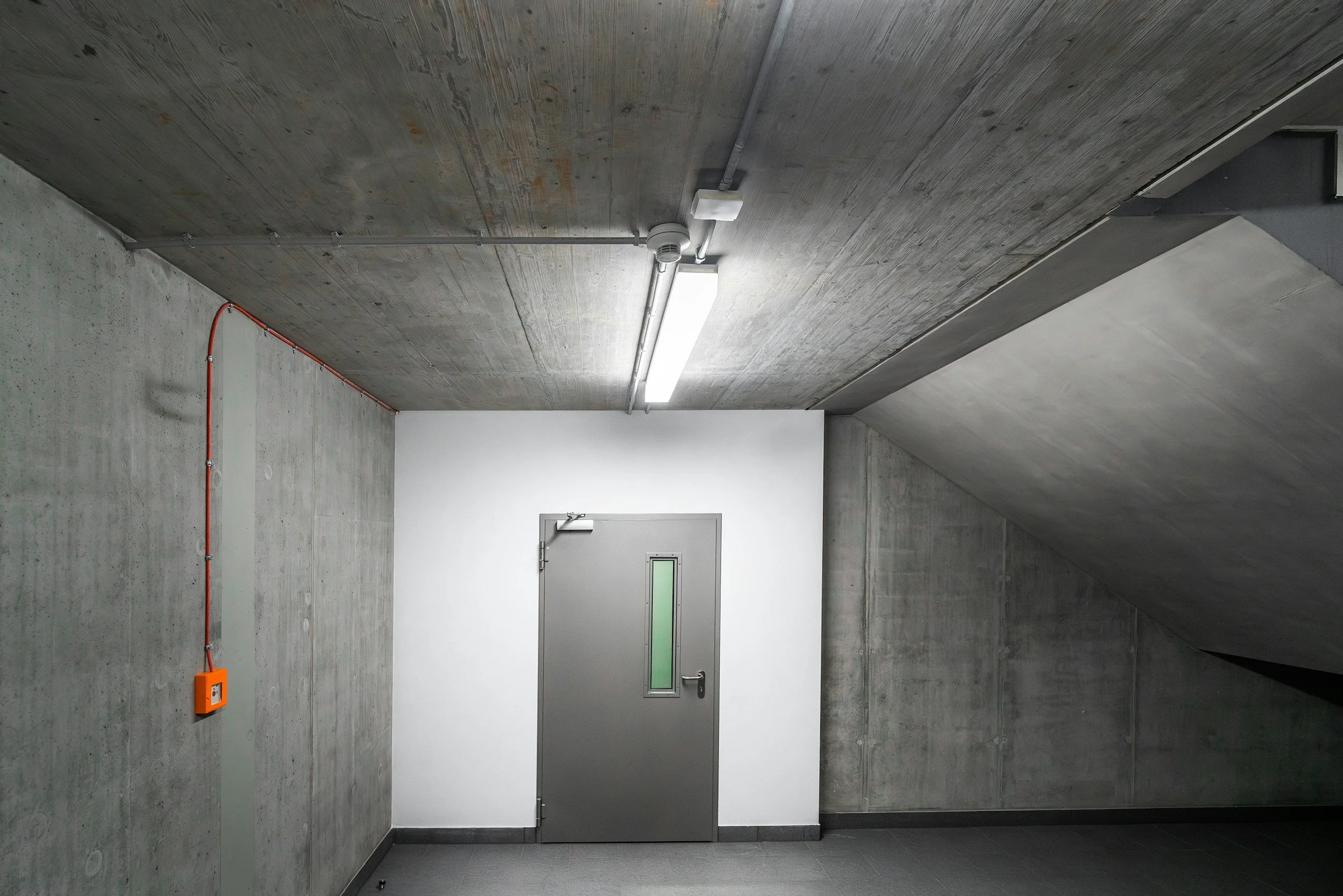 Concrete stairwell with a metal door and fluorescent light