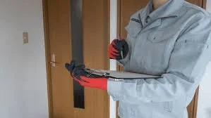Person in gray uniform with red gloves holding clipboard indoors