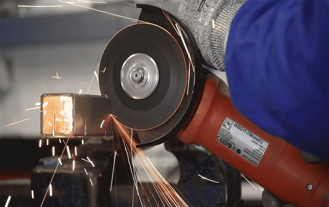 A person using an angle grinder to cut a metal pipe, with sparks flying.