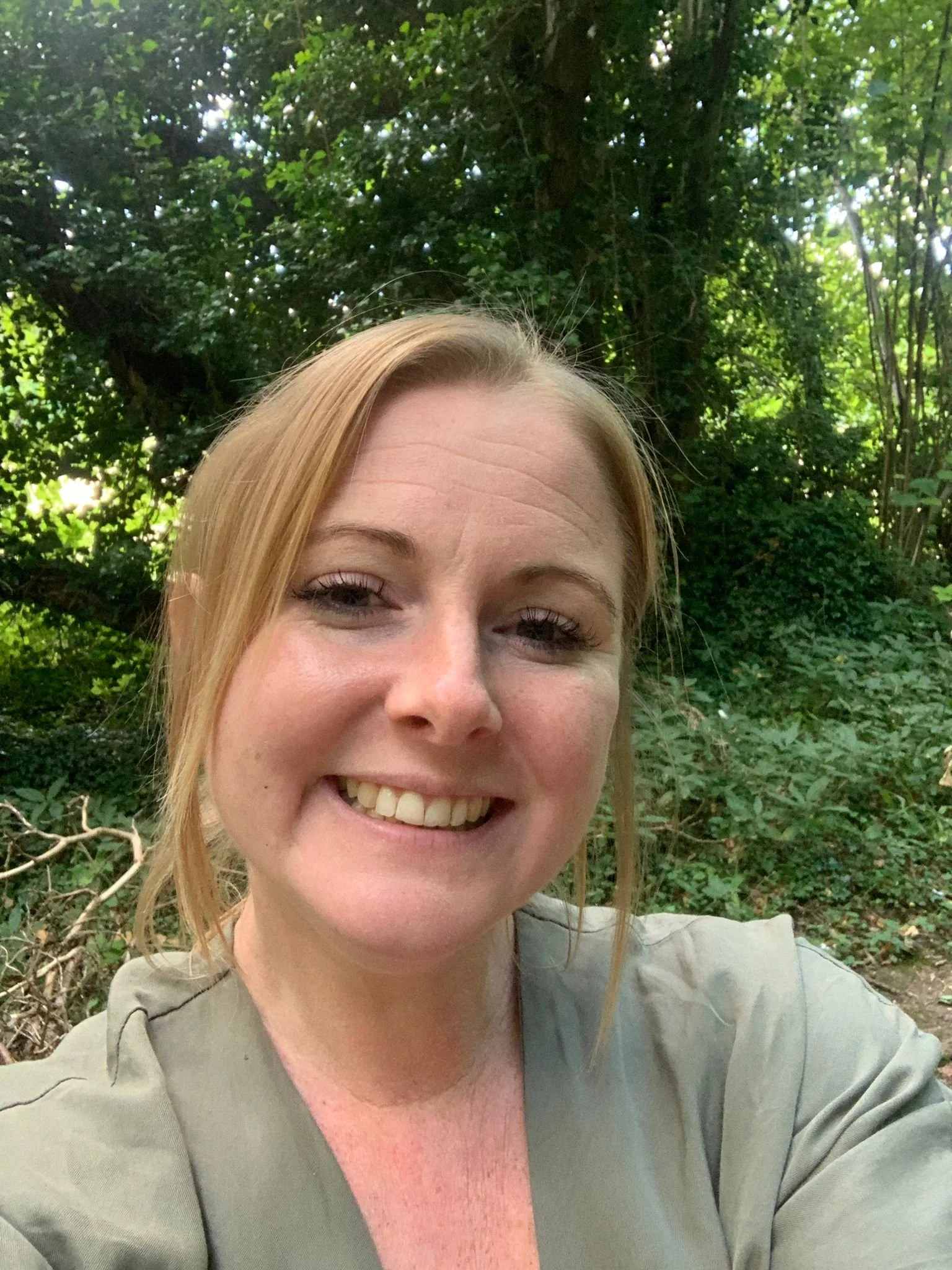 Smiling person taking a selfie in a green forest.