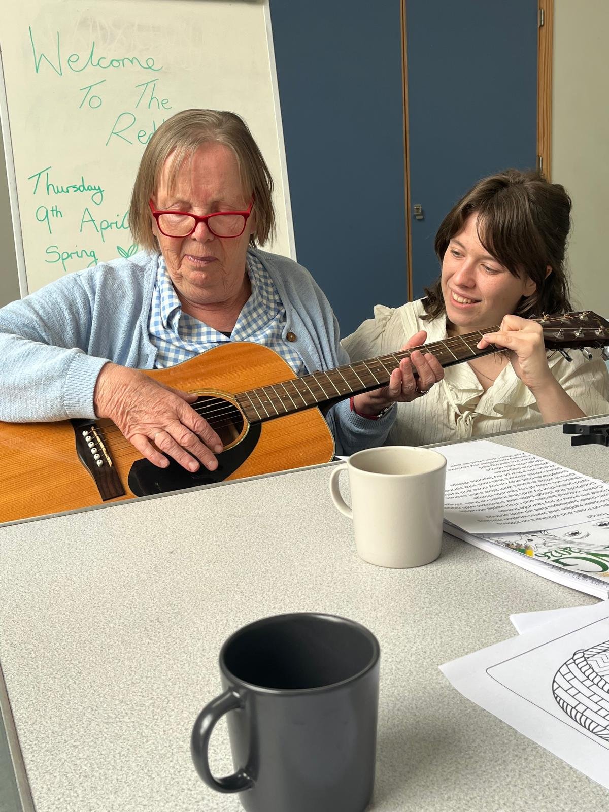 An older lady with a younger lady working together to learn the guitar.