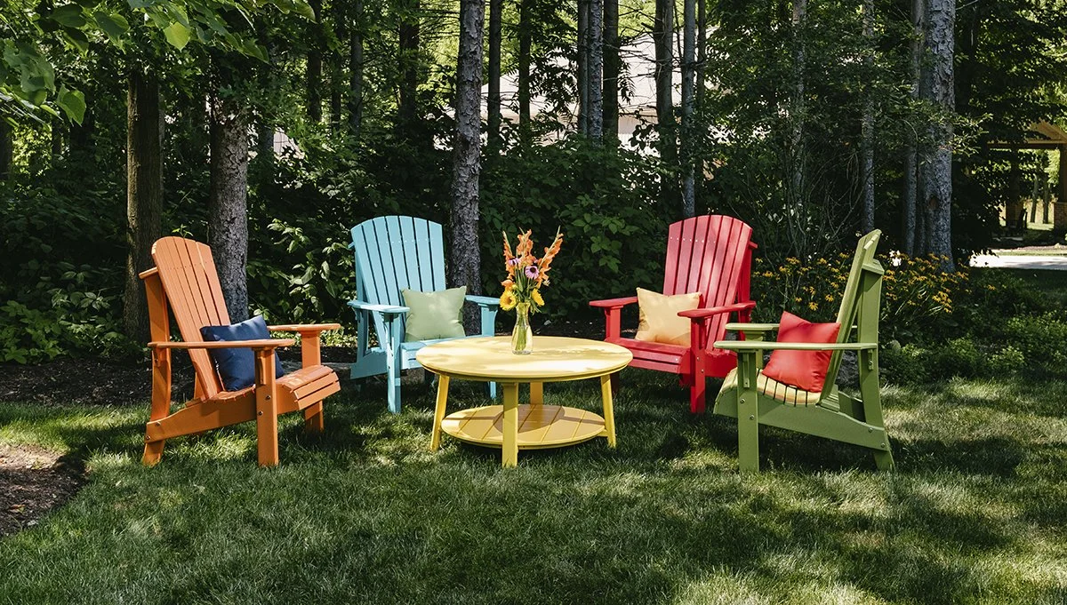 Colorful LuxCraft poly Adirondack chairs arranged around a round outdoor table in a shaded backyard