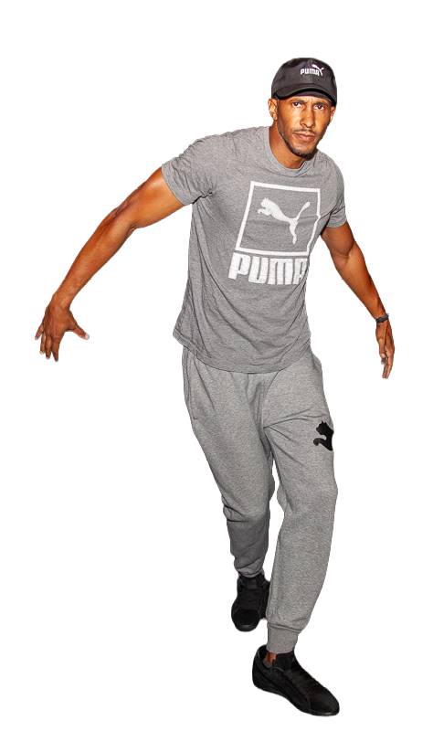 Leggs is wearing gray Puma t-shirt, matching sweatpants, black sneakers, and black Puma cap, in a classic Bronx rock "top rocking" stride step.