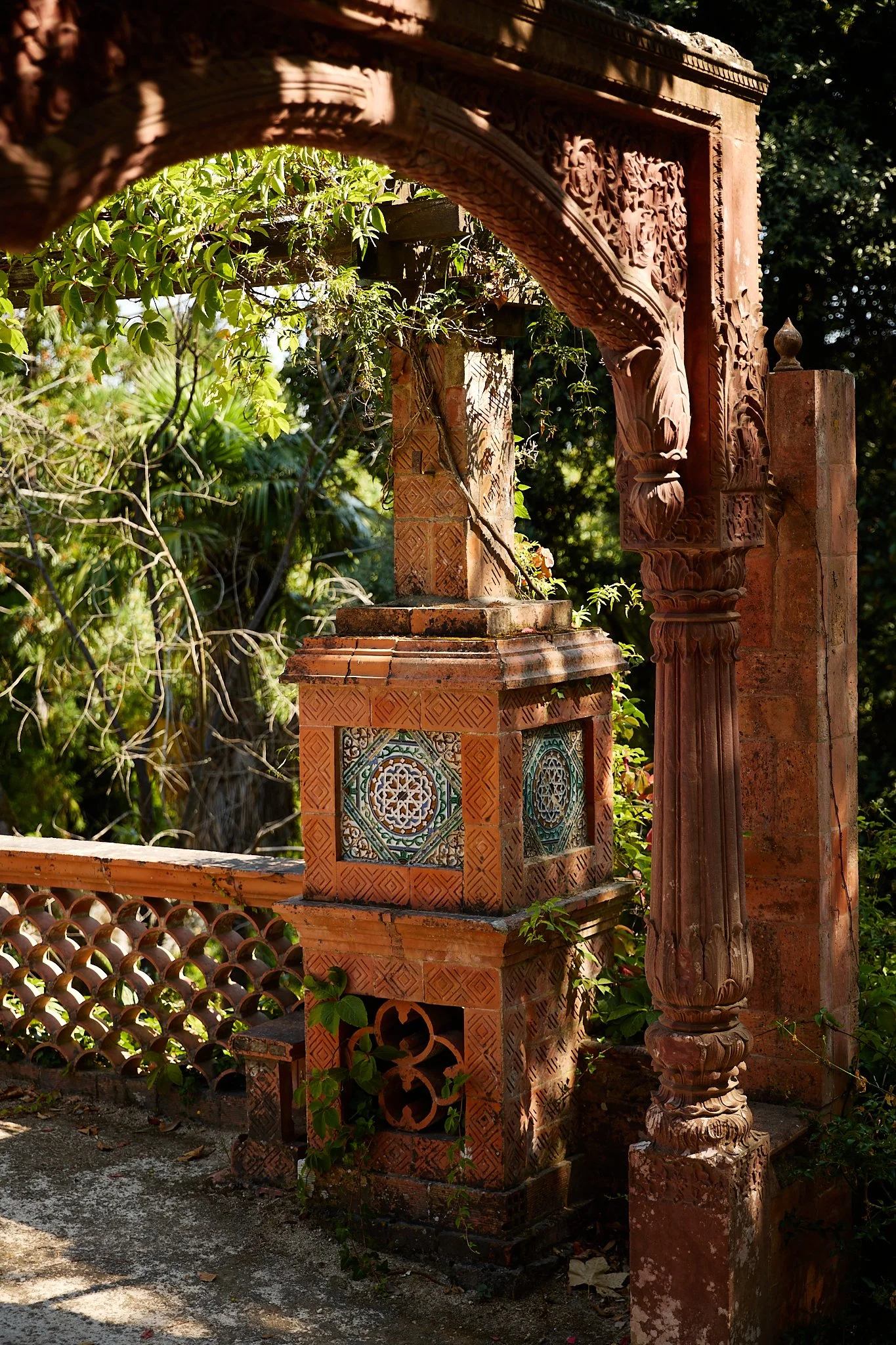Ornate terracotta garden arch and tiled pedestal surrounded by lush greenery