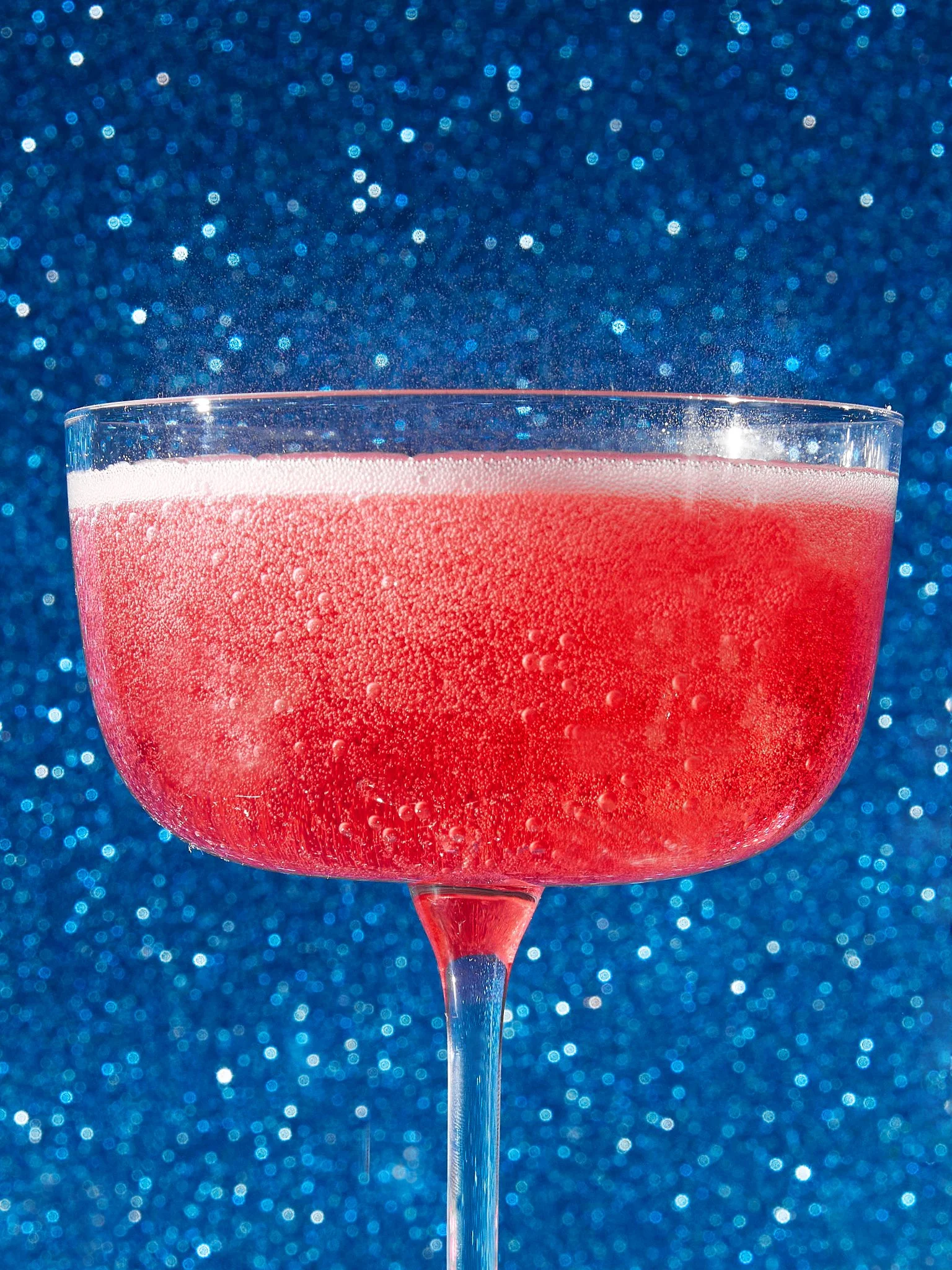 A pink cocktail in a coupe glass with a sparkling blue background.