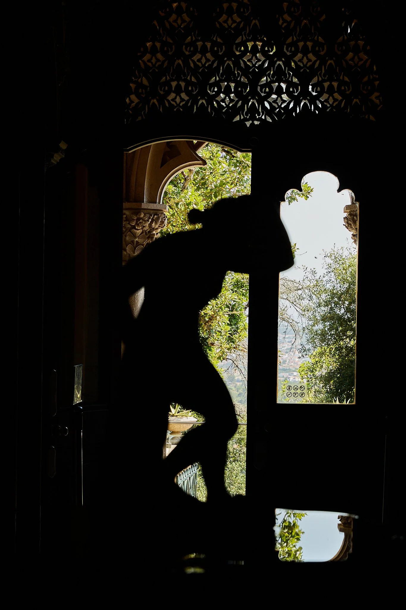 Silhouetted person standing inside an ornate Moorish-style doorway overlooking greenery and distant hills