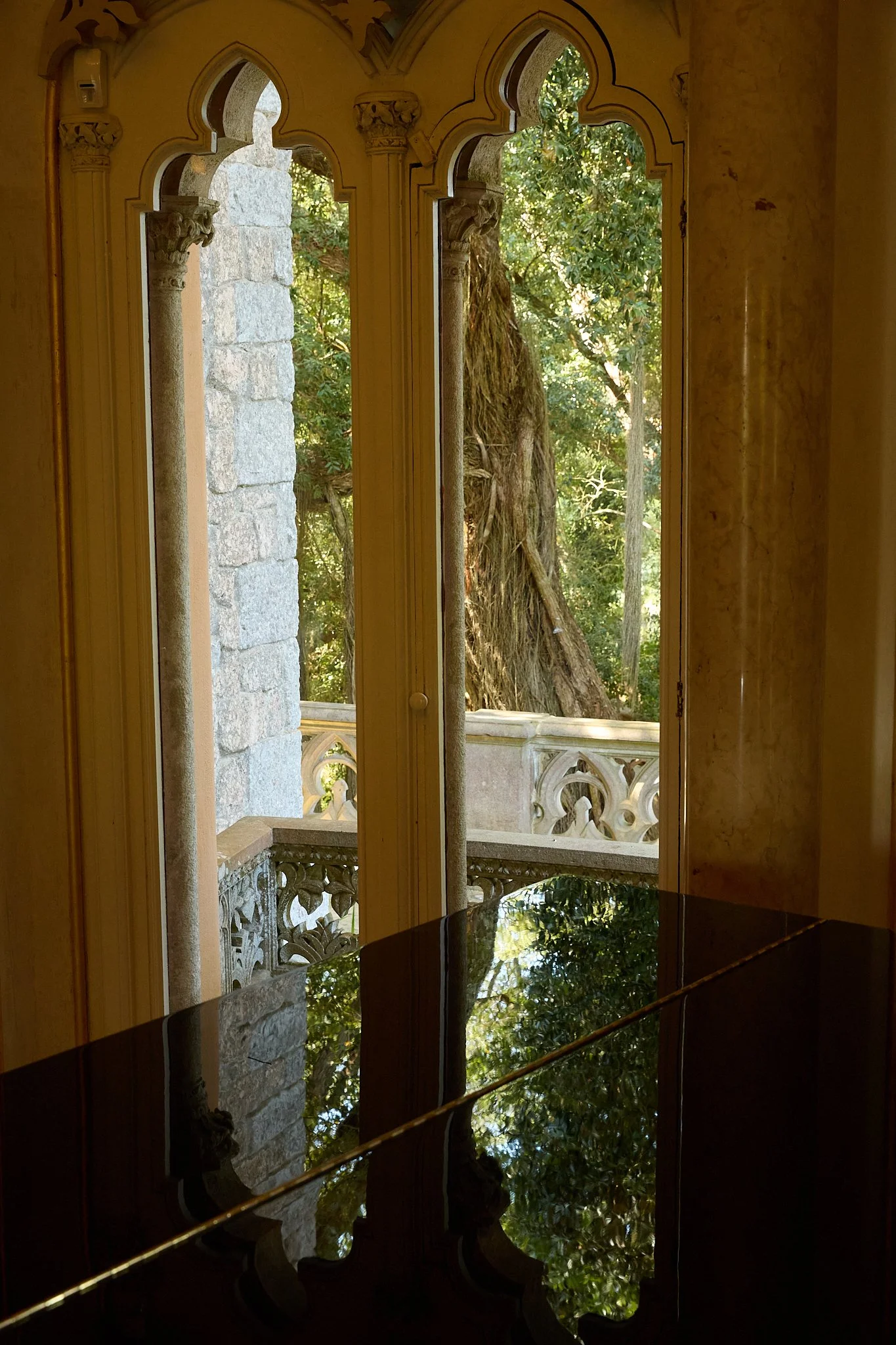 Ornate Gothic-style arched windows overlooking a leafy garden and stone balcony