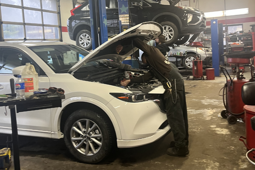 White car in an auto repair shop with a mechanic inspecting the engine. Vehicle Inspection in Burlington, VT At Girlington Garage