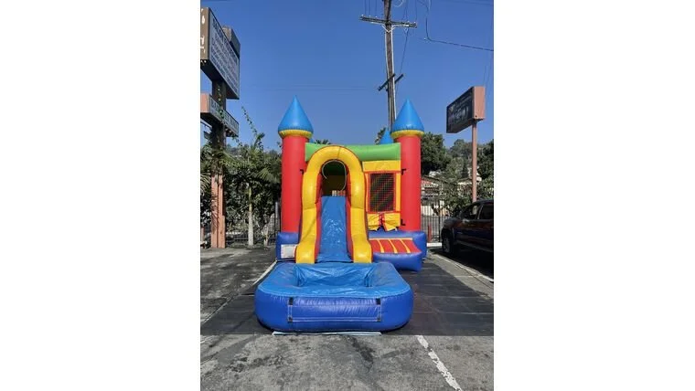 Colorful inflatable bounce house with slide and castle design on a parking lot pavement.