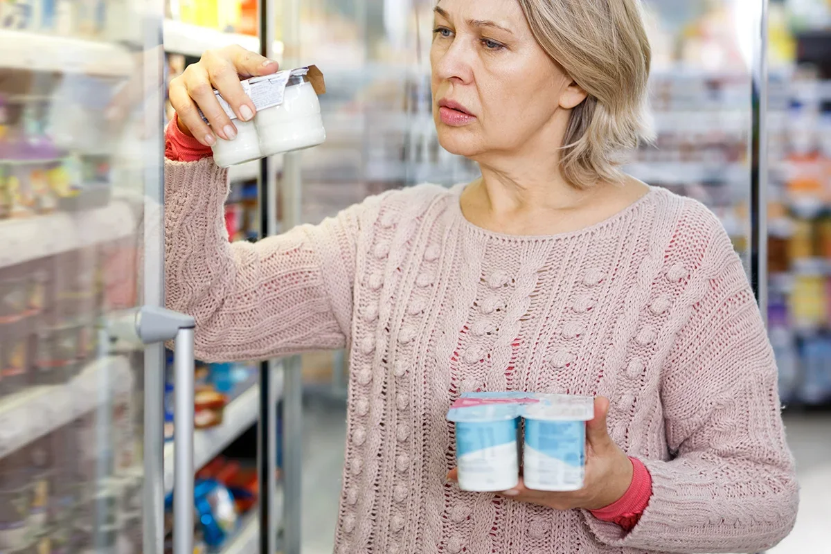 Shopper comparing yogurt products in a supermarket, representing how Customer journey research UK identifies key decision points, shopper motivations, and influences driving purchase choices.