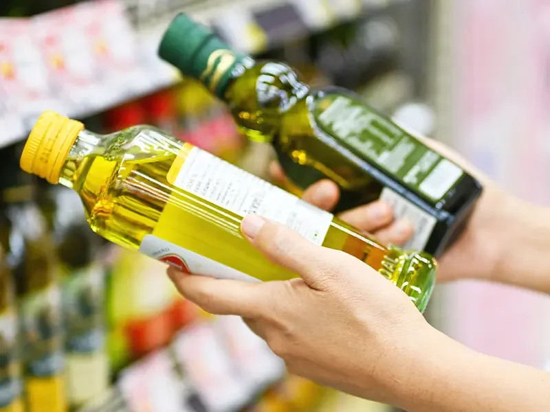 Close-up of shopper comparing two bottles of cooking oil on a supermarket shelf, highlighting how shopper behaviour research uncovers decision-making, product comparisons, and purchase choices through shopper behaviour research.