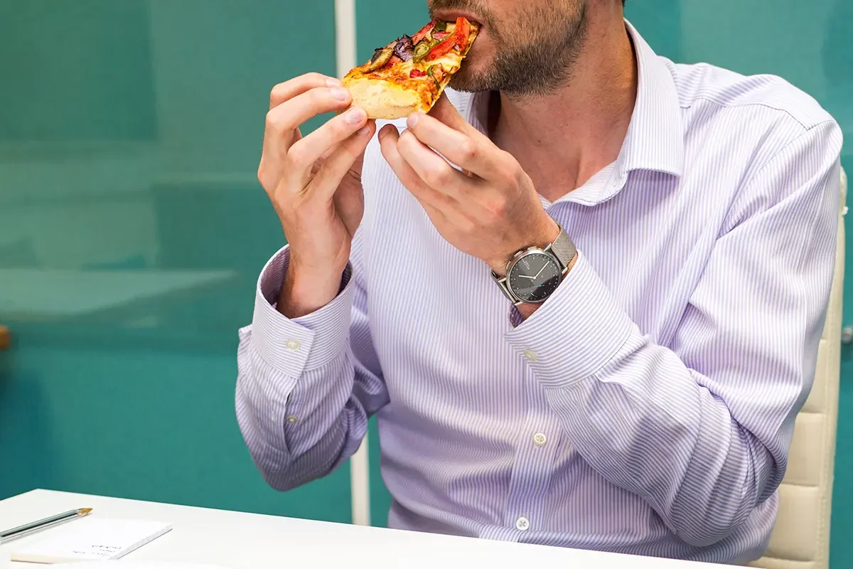 Man in a striped shirt tasting a slice of pizza during product testing and benchmarking, demonstrating how product testing and benchmarking evaluates flavour, texture, and consumer preferences.