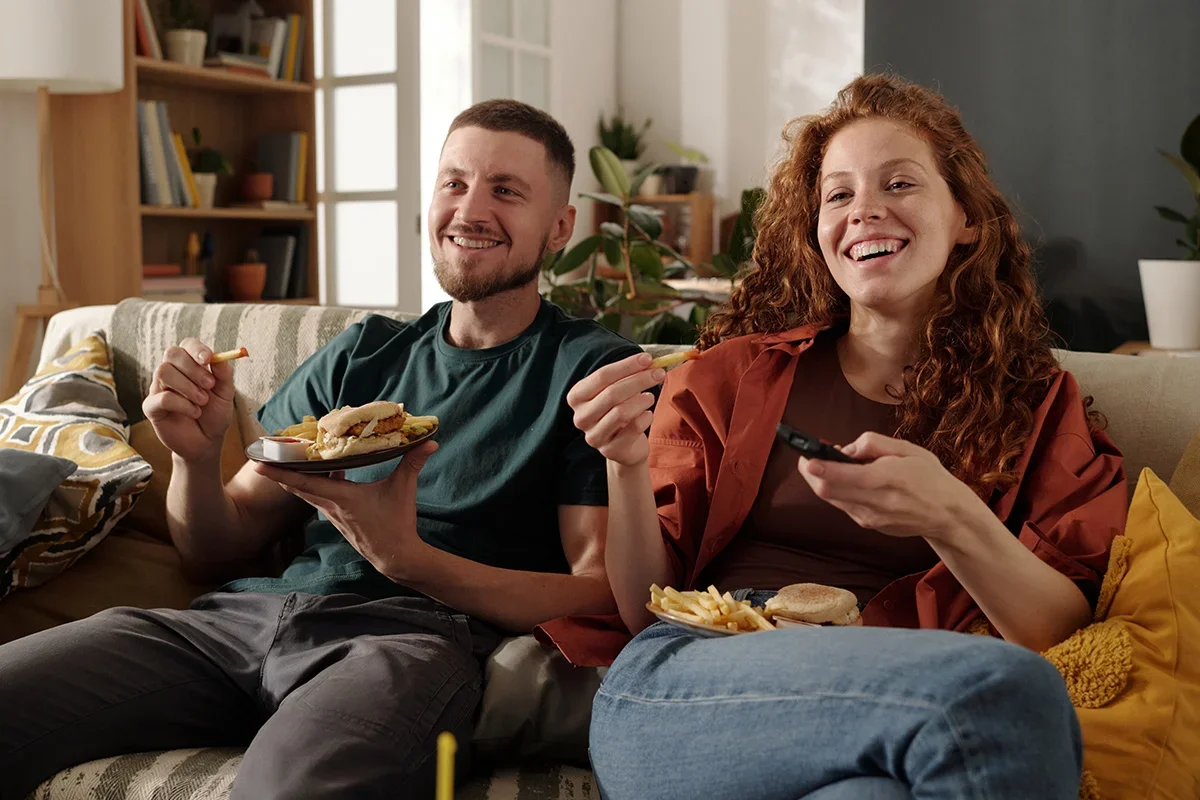 Young couple relaxing on the sofa eating takeaway food, representing how Consumer segmentation research UK identifies value-based lifestyle segments to help brands connect with different consumer motivations and behaviours.
