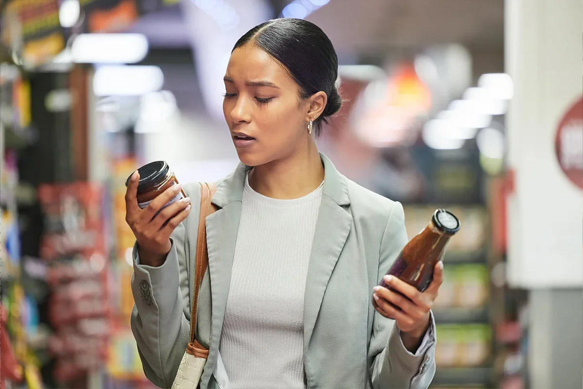 Shopper comparing two sauce products in a supermarket aisle, representing how Consumer segmentation research UK helps brands understand decision-making drivers, preferences, and pain points at the point of purchase.