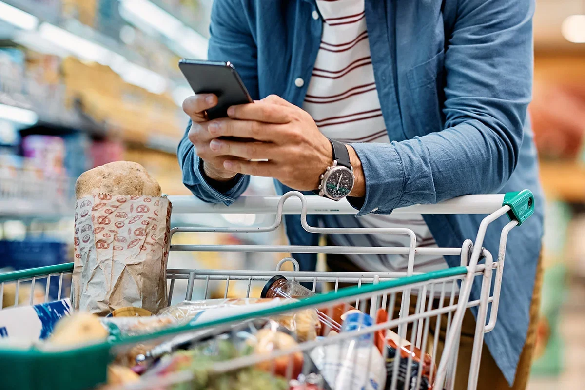 Shopper using a smartphone while grocery shopping, symbolising how Customer journey research UK captures real-time behaviour, decision-making, and digital touchpoints throughout the shopping experience.