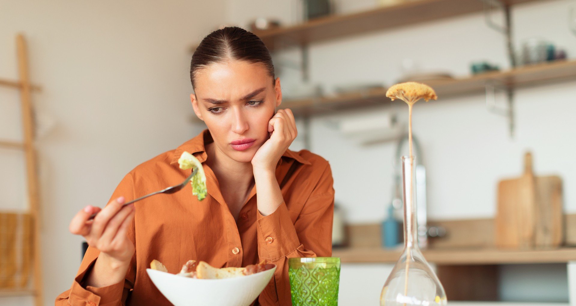 Woman looking disinterested while holding a forkful of salad, highlighting a loss of appetite or emotional disconnect from food.