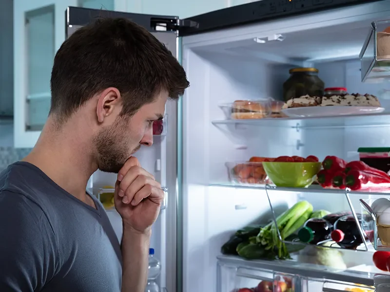 Man thoughtfully looking into an open fridge, symbolising decision-making moments at home that shopper behaviour research analyses, showing how shopper behaviour research uncovers choices, habits, and influences on consumer behaviour.
