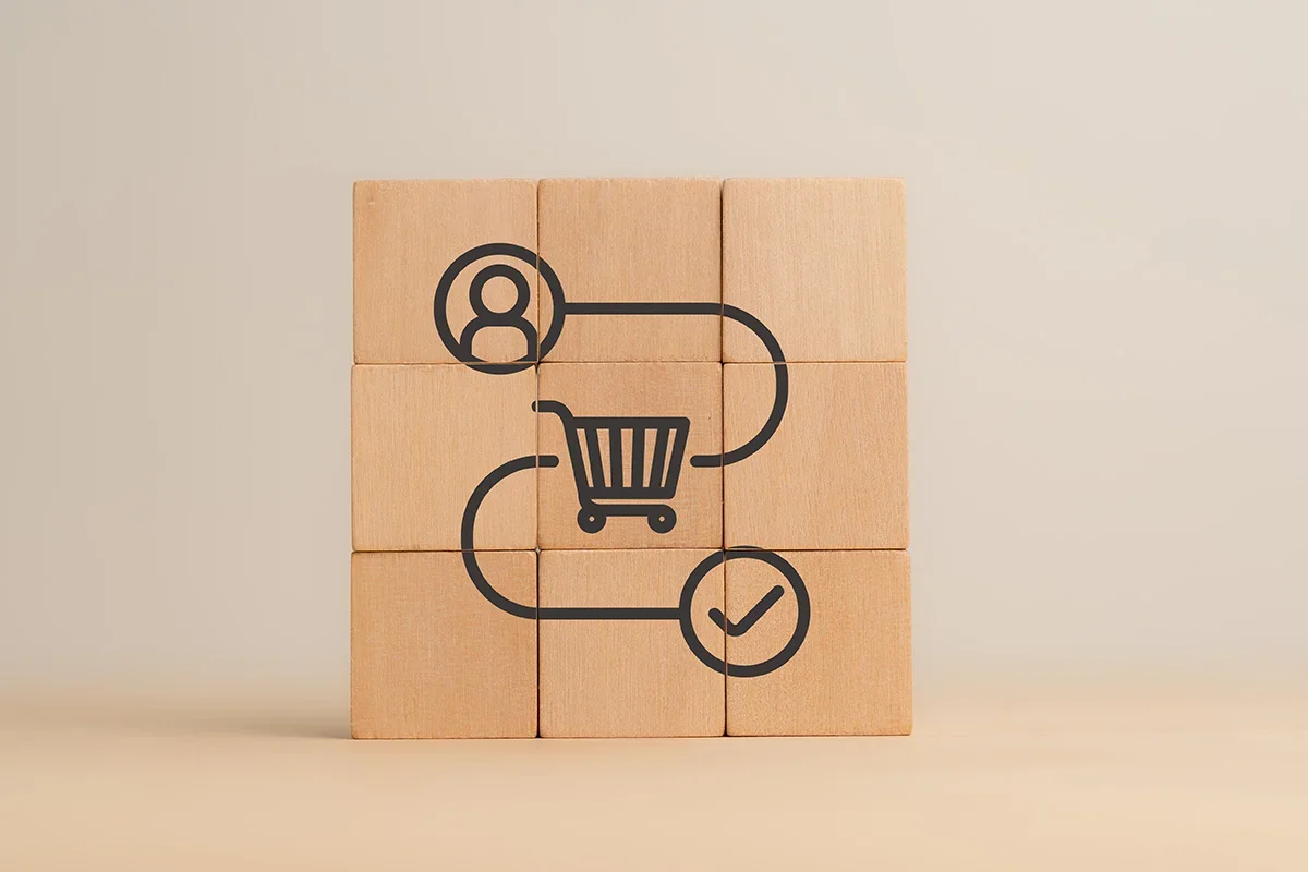 Illustration of a customer journey from person icon to shopping cart to checkmark on wooden blocks, symbolising how Customer journey research UK visualises decision pathways and key touchpoints to optimise the purchase experience.