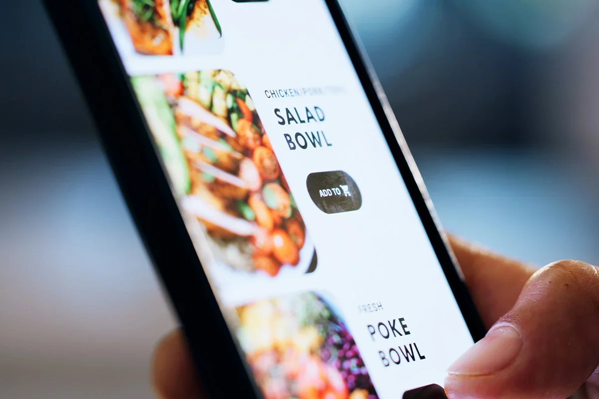 Close-up of a person using a mobile food ordering app, selecting a salad bowl, representing how Customer journey research UK analyses digital touchpoints and channel integration to enhance the customer experience and drive conversions.