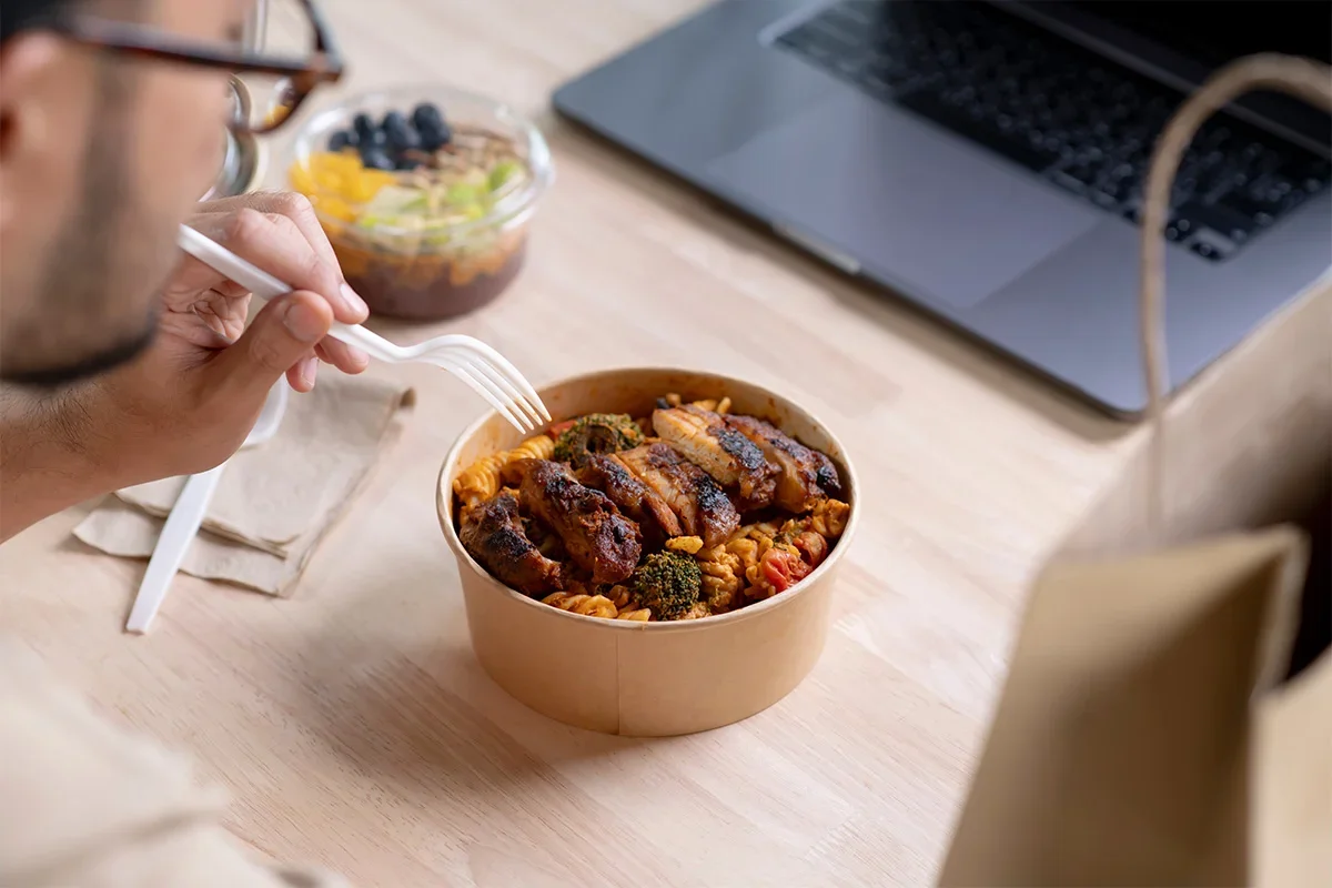 Person enjoying a takeaway meal while working on a laptop, symbolising how Consumer Closeness Research UK captures authentic consumer behaviour and real-life dining moments to deliver deeper insight into food experiences and brand engagement.