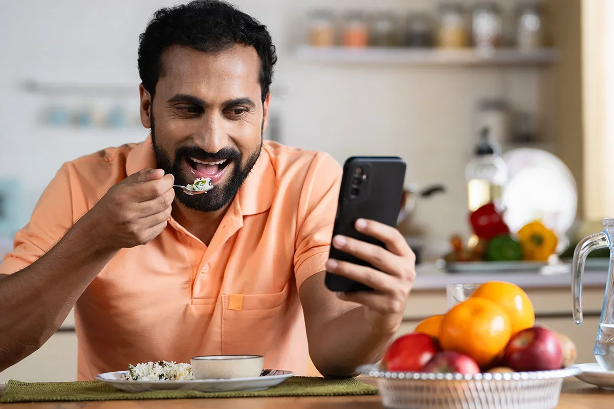 Man eating a meal while using his smartphone, representing Consumer Closeness Research UK capturing real consumer behaviour and in-the-moment dining experiences to help brands build authentic understanding of everyday eating habits.