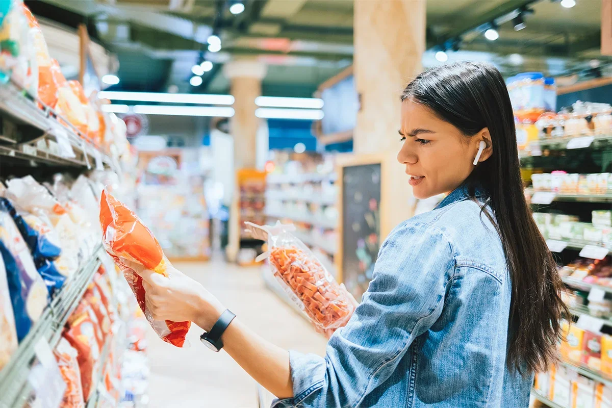 Shopper comparing two snack products on a supermarket aisle, representing how Customer journey research UK uncovers decision-making challenges, product confusion, and opportunities to improve customer clarity and purchase confidence.