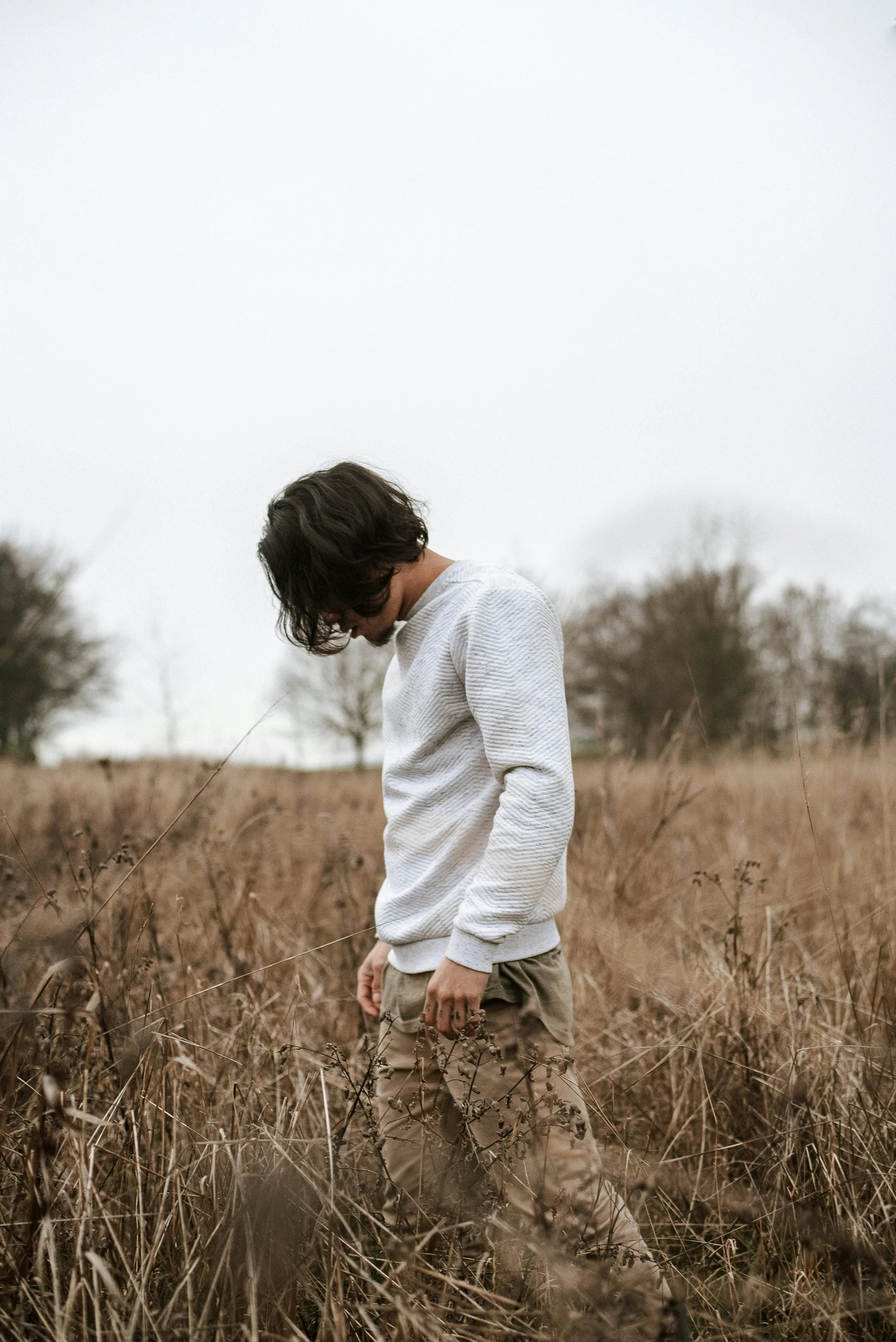 Person standing alone in an open field with head lowered, representing reflection and grief during a season of loss