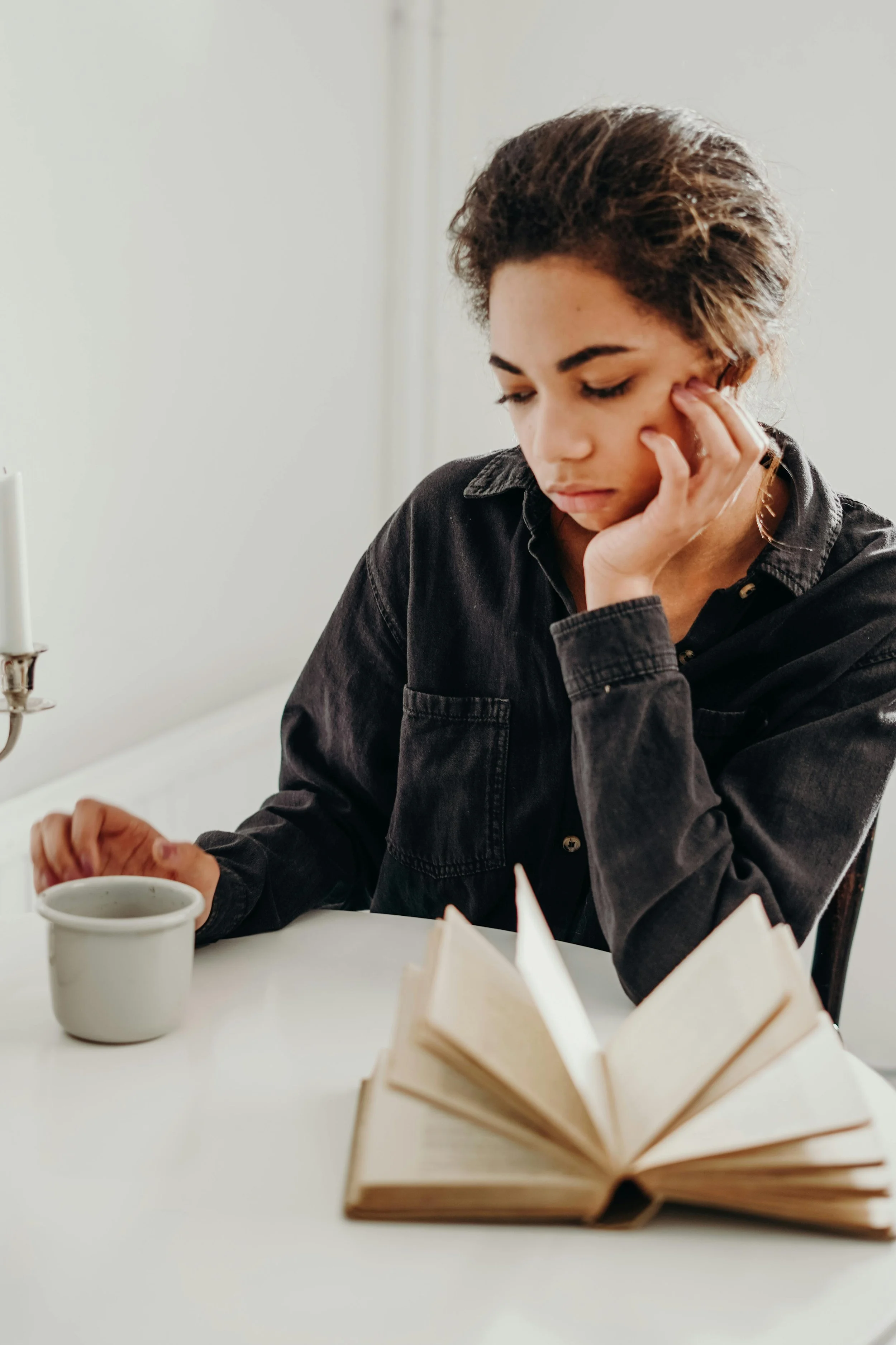 Woman sitting quietly at a table with a cup of tea in reflection, considering support through online anxiety counseling